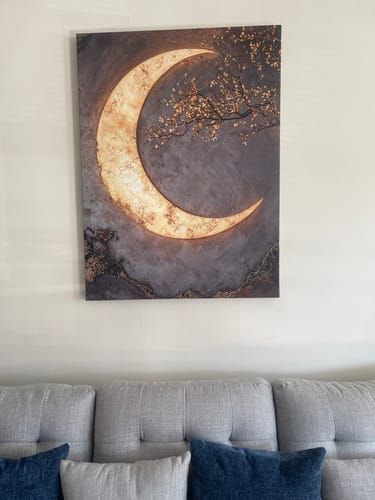 Customer's glowing Crescent Moon Canvas Wall Decor hanging on a wall above their light grey sofa.