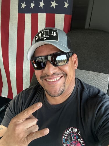 Customer smiling while wearing a personalized grey and black Texas Black Plate Hat in front of an American flag.