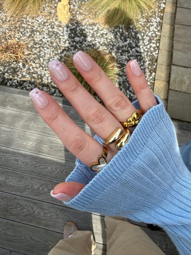 Customer's hand wearing the short, square In Bloom press-on nails with a delicate white flower design.