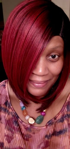 Customer wearing the Freetress VASHANTI wig in a vibrant red, asymmetrical bob style.