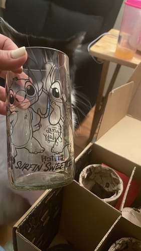 Cliente sosteniendo un vaso transparente de la colección Disney Stitch, con la caja abierta al fondo.