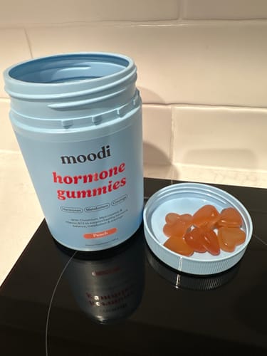 Reviewer's open blue bottle of Peach Hormone Gummies, with several heart-shaped gummies in the lid.