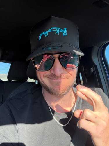 Reviewer wearing the black 80Eighty DCG87 Hat with a blue car outline inside a vehicle.