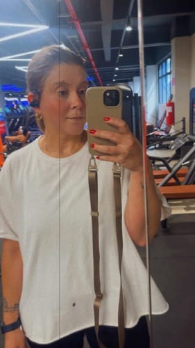 Avaliadora tira uma selfie no espelho mostrando a alça Aurora na cor areia presa ao seu celular.