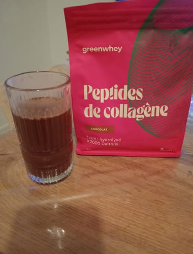 Client montrant son sachet rose de Peptides de Collagène saveur chocolat à côté de la boisson dans un verre.