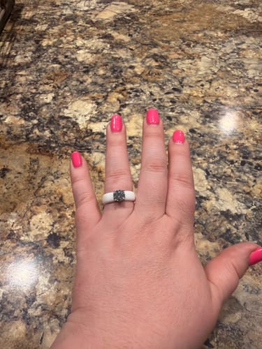 Customer's hand wearing the white silicone ring with a dark round solitaire stone against a granite countertop.