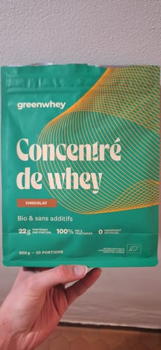 Client tenant dans sa main un sachet vert de Concentré de whey au chocolat.