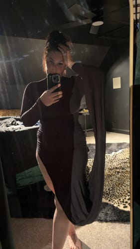 Reviewer in a mirror selfie wearing the dark Naked Draped Sleeve Maxi Dress, showing its high side slit and long draped sleeve.