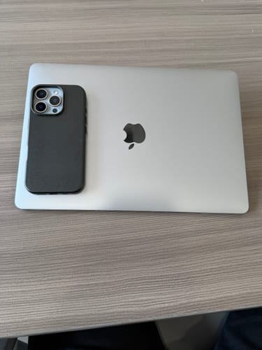 Customer's black Signature Leather Magsafe Case on an iPhone, placed on top of a closed laptop on a desk.