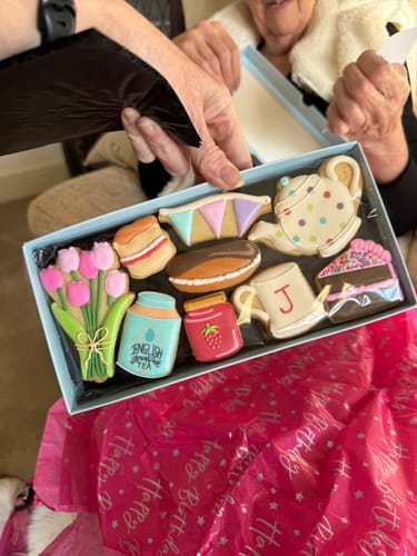 A person holding the open Afternoon Tea Deluxe Biscuit Box, showing the decorated biscuits for a birthday gift.