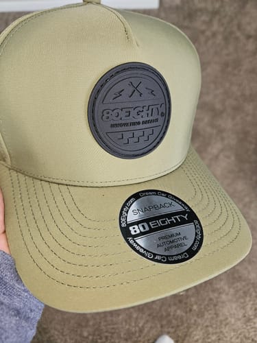 Customer holding the light green 80Eighty Vert Hat, showing the front with its black logo patch and new sticker on the brim.