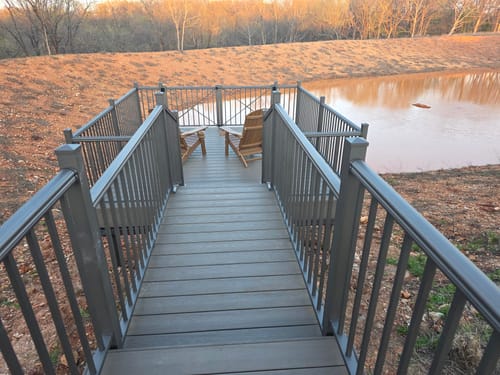 Customer's two assembled Folding Adirondack Chairs on a grey deck overlooking a pond.