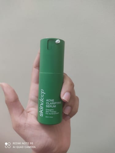 Reviewer holding the green bottle of ACNE CLARIFYING SERUM in their hand.