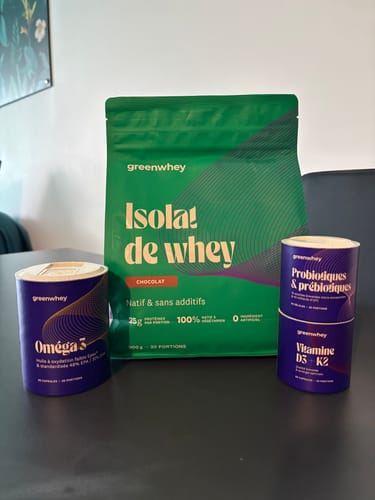 Photo d'un client montrant son pot d'Oméga 3 parmi d'autres produits Greenwhey posés sur une table.