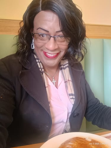 Customer smiling while wearing the dark, wavy New Born Free Cutie Collection Full Wig.