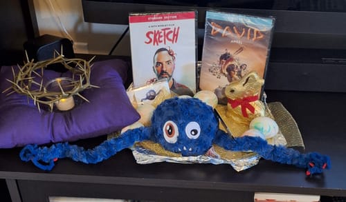 Customer's blue SKETCH Dave Plushie with its long arms spread out, shown among other Easter basket gifts on a shelf.