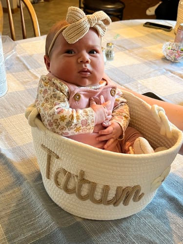 Reviewer's white personalized knitted basket with 'Tatum' on the side, holding a newborn baby.