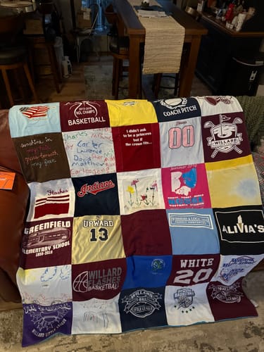 Reviewer's colorful Project Repat T-Shirt Quilt made of many different shirts, displayed on a couch.