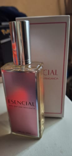 Un cliente muestra el frasco del perfume ESENCIAL con etiqueta rosa junto a su caja blanca.