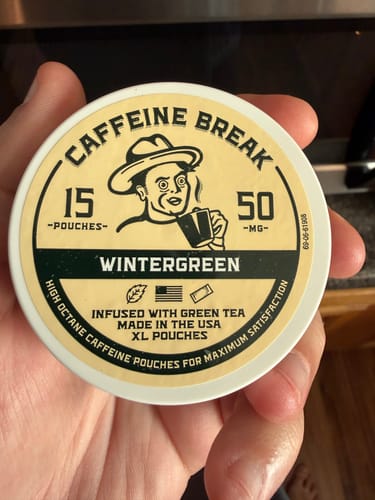 A customer holds up the lid of a tin of Wintergreen Caffeine Pouches to show the product's label.