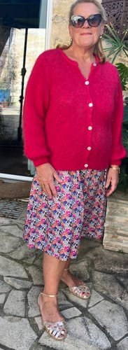 Cliente portant le Gilet Sélène duveteux rose vif sur une jupe à motifs.