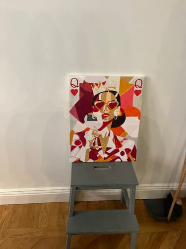 Customer's completed 'The queen' paint-by-number canvas displayed on a small grey stool against a wall.
