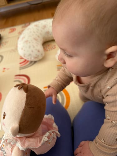 Customer's baby reaching out to touch the soft Personalized Daisy Baby Girl doll on a person's lap.