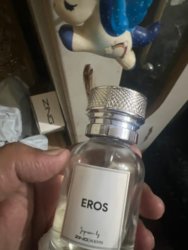 A customer holding the clear glass bottle of EROS fragrance with its textured silver cap.