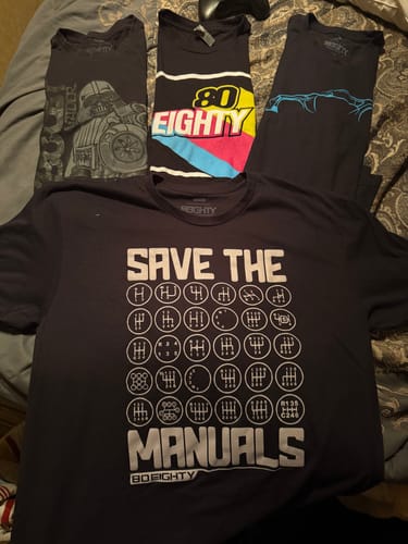 Customer's black 'Save The Manuals' shirt laid out with their collection of other 80Eighty shirts.
