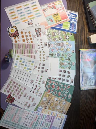 Reviewer shows the large assortment of sticker sheets from the Oopsie Mystery Bag fanned out on a purple mat.
