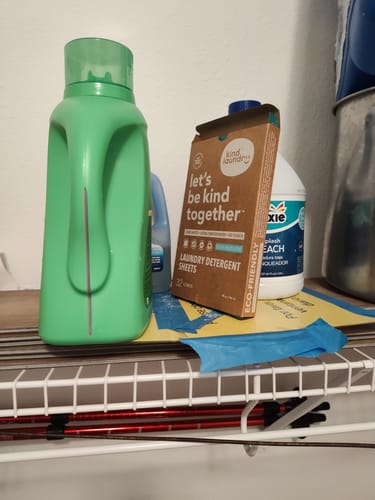 Customer's box of Laundry Detergent Sheets on a shelf next to a large, traditional plastic detergent jug.