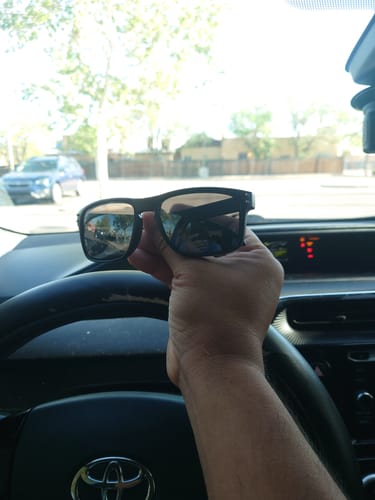 A reviewer holding up the black chrome 80Eighty Polarized Sunglasses from the driver's seat of a car.