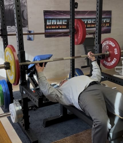 Customer bench pressing with red and yellow Strength Shop Calibrated Plates on a barbell in a home gym power rack.
