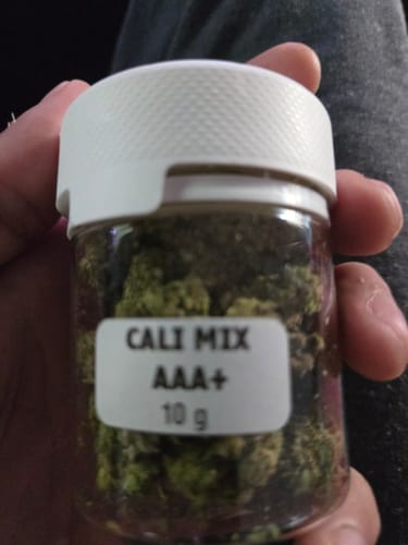 Customer holding a clear 10g jar of CALI MIX AAA+ premium flowers, showing the product and packaging.