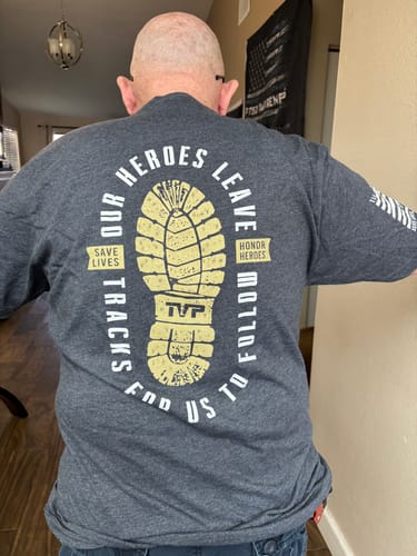 Customer from behind wearing the grey T.V.P. Elite Membership t-shirt, showing the back graphic with a large boot print.