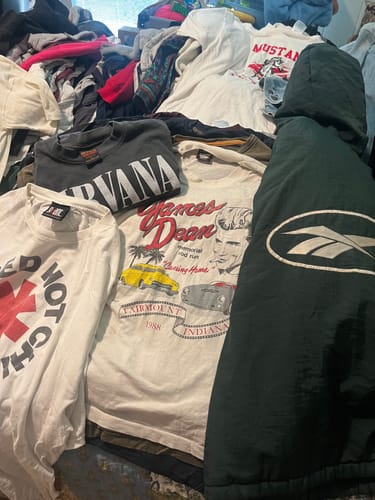 Customer's large pile of tees from the Premium Tees Bale, showing Nirvana, James Dean, and Red Hot Chili Peppers shirts.