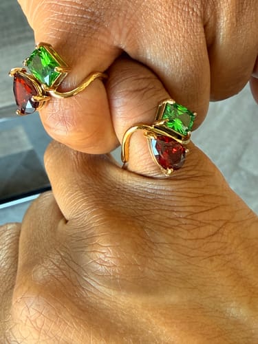 Customer's hands in a pinky promise, each wearing a matching Navae Birthstone Ring with red and green stones.