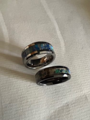 Reviewer's two black Titanium Carbide Rings with colorful opal and cremation ash inlays on a white surface.