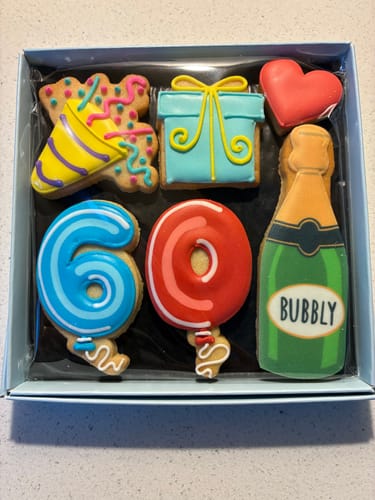 Customer's open Birthday Balloon Biscuit Box with decorated biscuits for a 60th birthday, including a bubbly bottle and a gift.