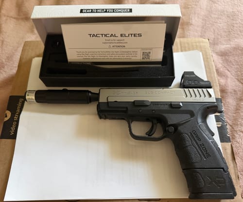 Reviewer showing the Site Right™ 2.0 - Boresighter inserted into a handgun, with its open box in the background.