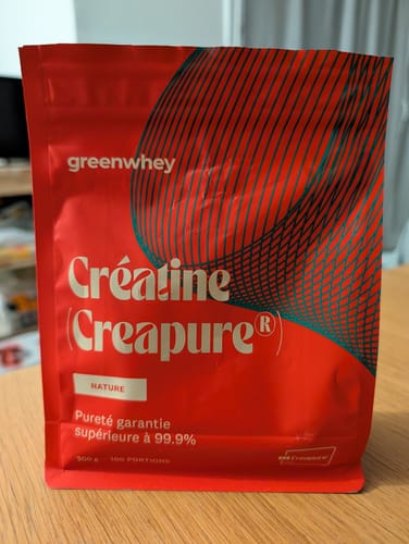 Un client montre son sachet rouge de Créatine Creapure®, posé sur une table.