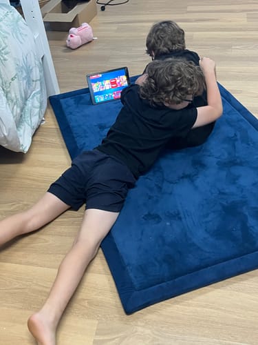 Customer's two children lying on a royal blue Mellow Mat while playing on a tablet.
