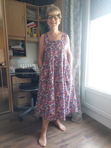 Une cliente souriante porte la Robe Solène à imprimé fleuri, debout à l'intérieur, les mains dans les poches.