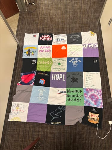 Reviewer's finished Premium T Shirt Quilt, made from many colorful shirts, spread out on a floor.