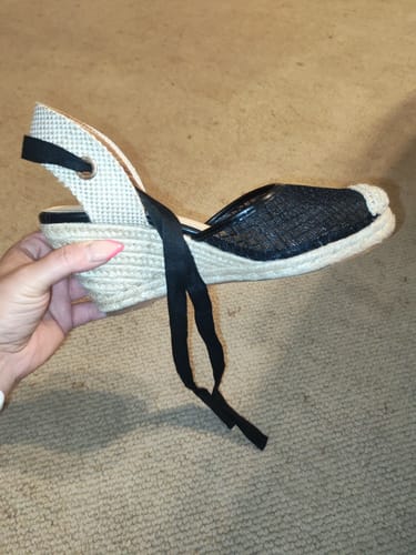 Customer holding a black Miss Black Jojo 14 Wedge shoe with a see-through mesh upper and tie-up strap.