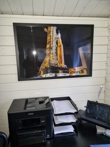 Reviewer's 'Back to the Pad - SLS' print in a black frame, hanging on a wall above an office desk.