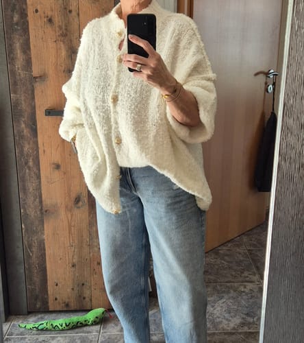 Kundin trägt den übergroßen Bouclé Cardigan 'CozyGlam' zu einer Jeans.
