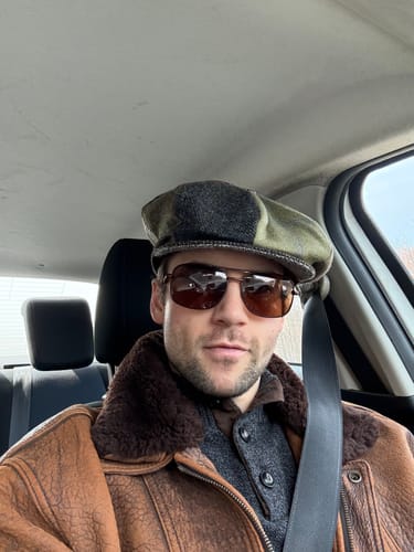 Customer wearing the Eight Piece Cap Patchwork Tweed with green and grey panels in a car.