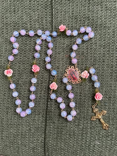 Customer's beautiful Rose-Accented Rosary with iridescent pastel beads and pink roses on a green textured surface.