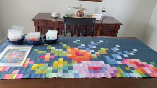 Customer's Tilda Embroidery Flower Precut Quilt Kit in progress, showing a colorful pixelated panel on a table with fabric squares.